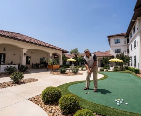 Senior Man Playing Golf on Outdoor Green at Assisted Living Facility Senior Man Playing Golf on Outdoor Green at Assisted Living Facility