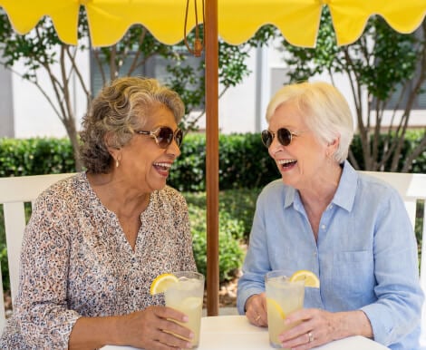 Two Elderly Women Socializing Outdoors with Drinks at Assisted Living Facility Two Elderly Women Socializing Outdoors with Drinks at Assisted Living Facility